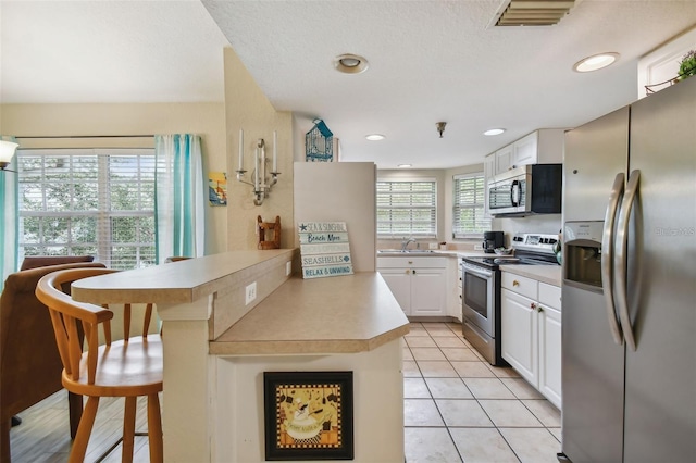 kitchen featuring visible vents, appliances with stainless steel finishes, a peninsula, light countertops, and a sink