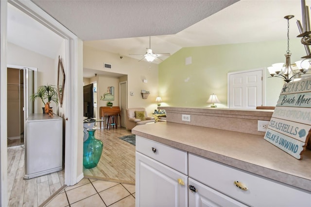 interior space with light wood finished floors, lofted ceiling, light countertops, white cabinetry, and ceiling fan with notable chandelier