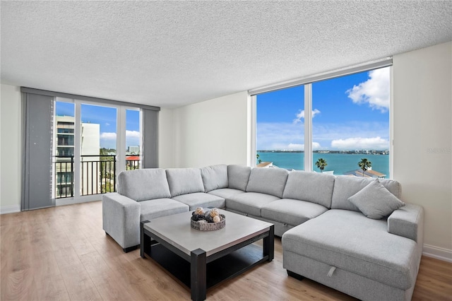 living room with a textured ceiling, a water view, wood finished floors, baseboards, and floor to ceiling windows