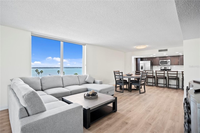 living room with a water view, light wood finished floors, visible vents, and a textured ceiling