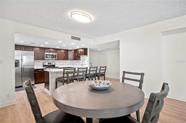 dining area featuring light wood-type flooring, baseboards, visible vents, and a textured ceiling