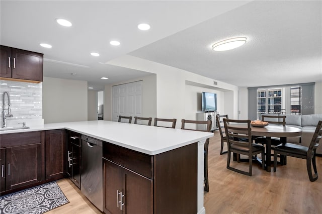 kitchen featuring tasteful backsplash, dishwasher, light wood-style floors, a kitchen bar, and a sink