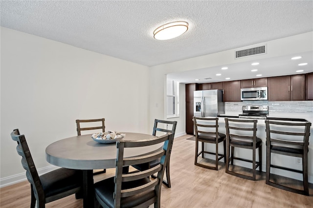 dining space with visible vents, light wood-style flooring, baseboards, and a textured ceiling