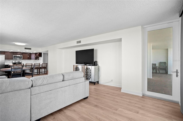 living area with light wood finished floors, baseboards, visible vents, and a textured ceiling