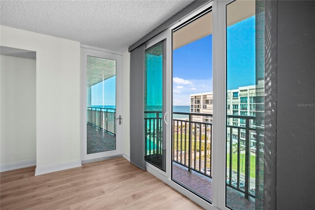 doorway to outside featuring a textured ceiling, baseboards, and wood finished floors