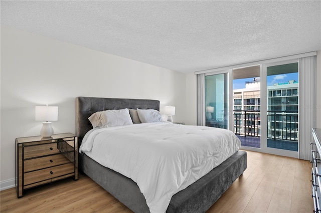 bedroom with light wood-type flooring, access to exterior, a wall of windows, and a textured ceiling