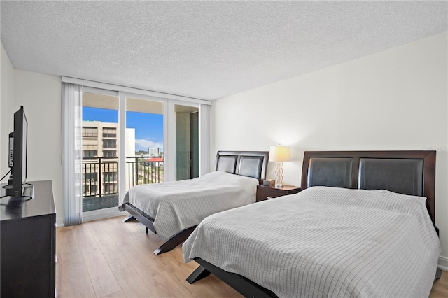 bedroom featuring access to exterior, expansive windows, a textured ceiling, and light wood finished floors