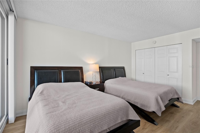 bedroom with a textured ceiling, a closet, light wood-style flooring, and baseboards