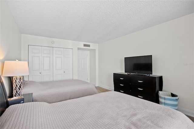 bedroom featuring baseboards, a textured ceiling, visible vents, and a closet