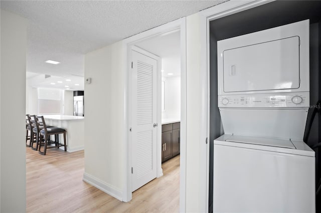 laundry area featuring stacked washer and dryer, a textured ceiling, light wood-type flooring, laundry area, and baseboards