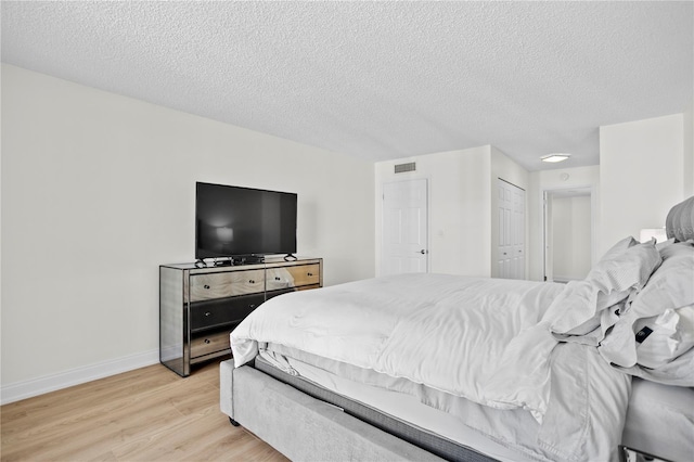 bedroom with light wood-style floors, visible vents, a textured ceiling, and baseboards