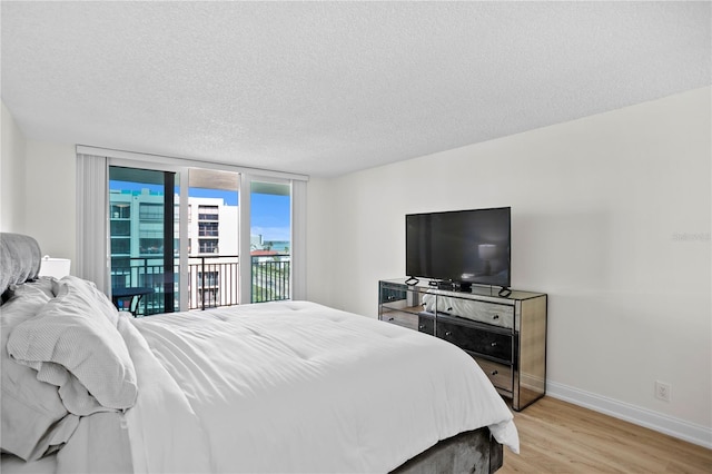 bedroom featuring a textured ceiling, baseboards, light wood-style floors, access to outside, and a wall of windows