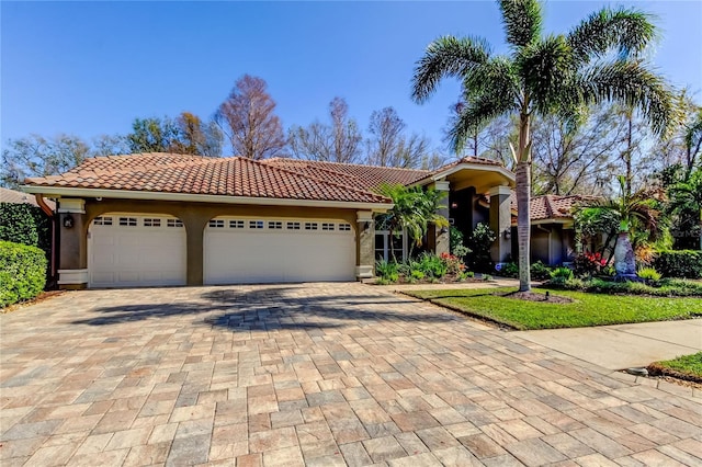 mediterranean / spanish-style home featuring a garage, a tiled roof, decorative driveway, and stucco siding