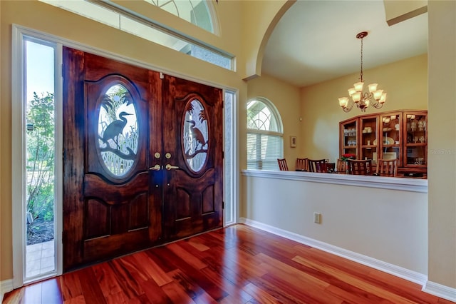 foyer with baseboards, arched walkways, wood finished floors, and an inviting chandelier