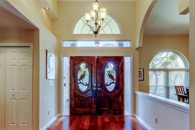 entryway with a chandelier, arched walkways, baseboards, and wood finished floors