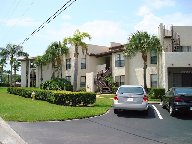 view of property with uncovered parking, a front yard, stucco siding, and stairs