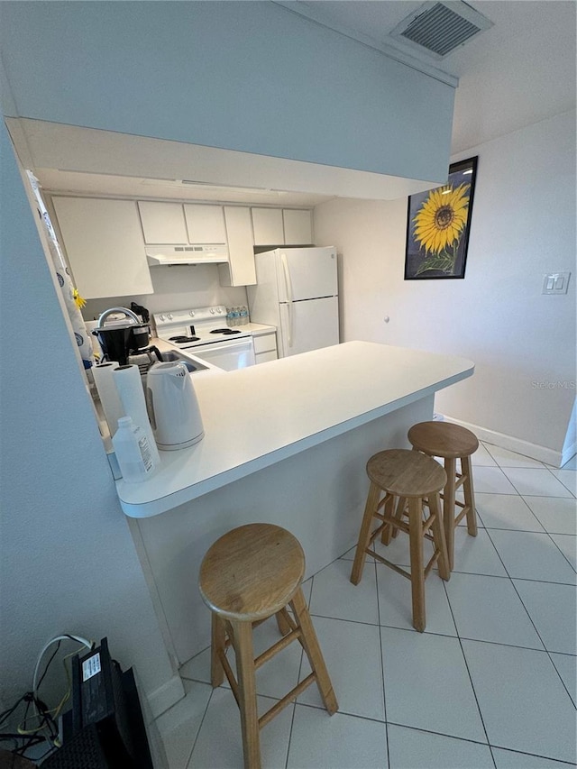 kitchen with under cabinet range hood, white appliances, visible vents, white cabinets, and a kitchen bar