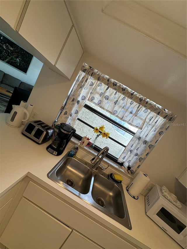 kitchen featuring light countertops, a sink, and white microwave