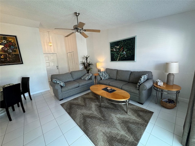 living area with light tile patterned floors, baseboards, a ceiling fan, and a textured ceiling