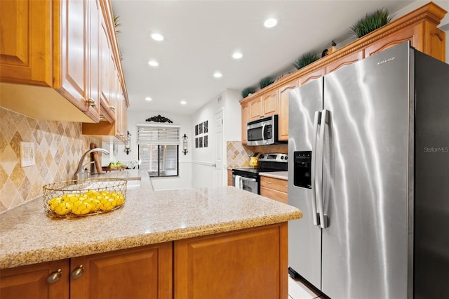 kitchen featuring stainless steel appliances, brown cabinetry, a sink, light stone countertops, and a peninsula