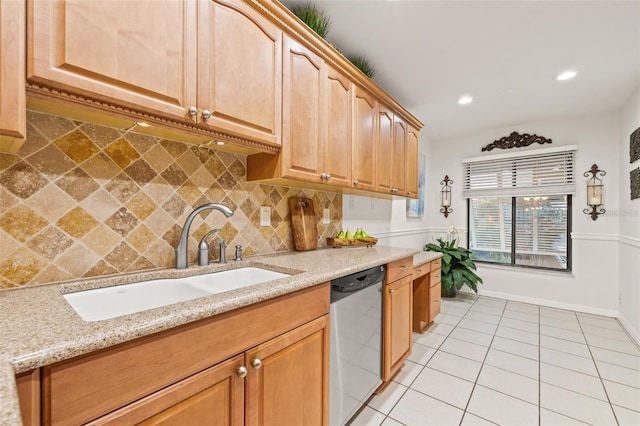 kitchen with light stone counters, light tile patterned flooring, a sink, stainless steel dishwasher, and decorative backsplash