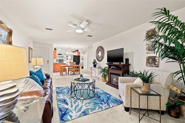 living room featuring a glass covered fireplace and ceiling fan with notable chandelier