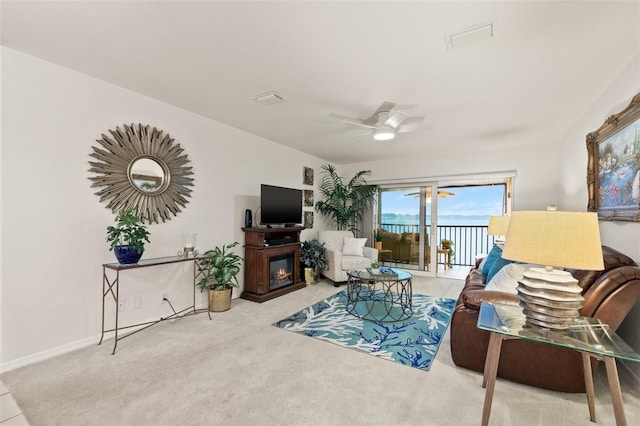 living room featuring visible vents, baseboards, light colored carpet, a glass covered fireplace, and ceiling fan