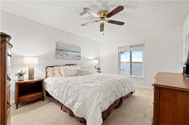 bedroom with a water view, a ceiling fan, light carpet, a textured ceiling, and baseboards