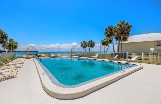 pool featuring a patio, a water view, and fence