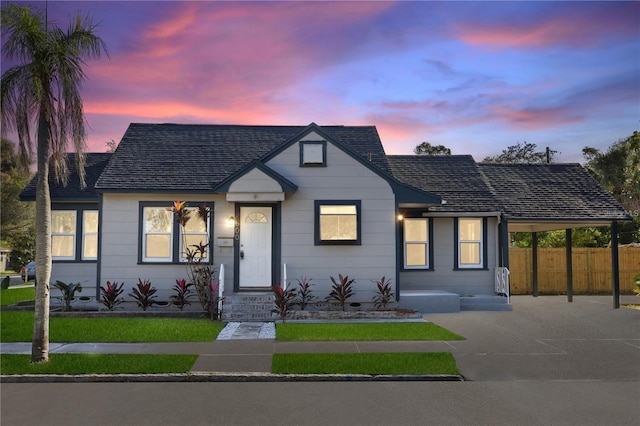 bungalow-style house featuring a shingled roof, an attached carport, fence, and driveway