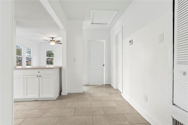 hall with light tile patterned floors, arched walkways, attic access, and baseboards