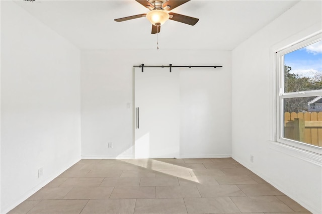 spare room featuring light tile patterned floors, a barn door, and a ceiling fan