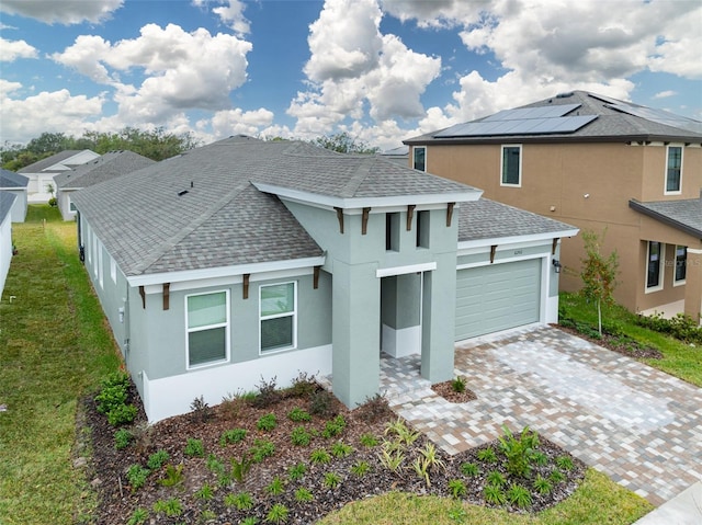 view of front facade with an attached garage, a shingled roof, decorative driveway, roof mounted solar panels, and stucco siding