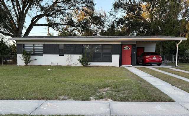 view of front facade featuring concrete block siding, a carport, and a front yard