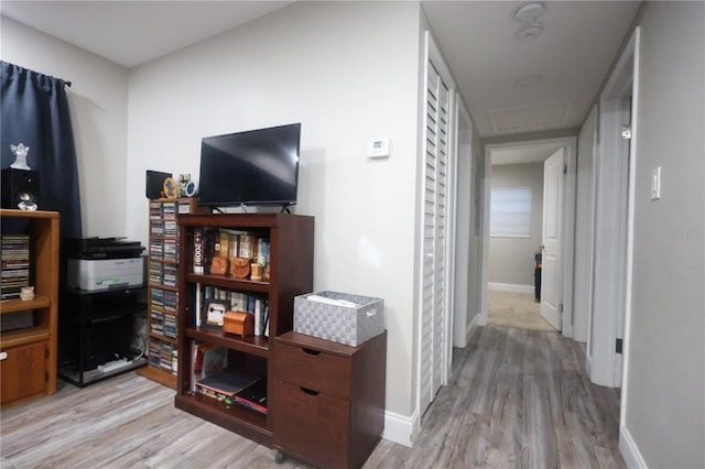 hall featuring light wood-style flooring, attic access, and baseboards