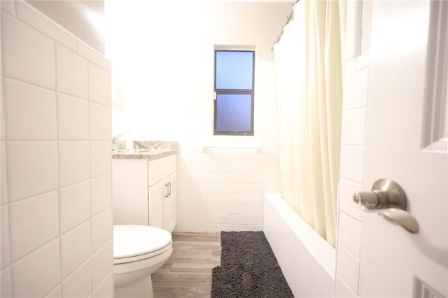 bathroom with toilet, wood finished floors, vanity, tile walls, and shower / bathtub combination with curtain