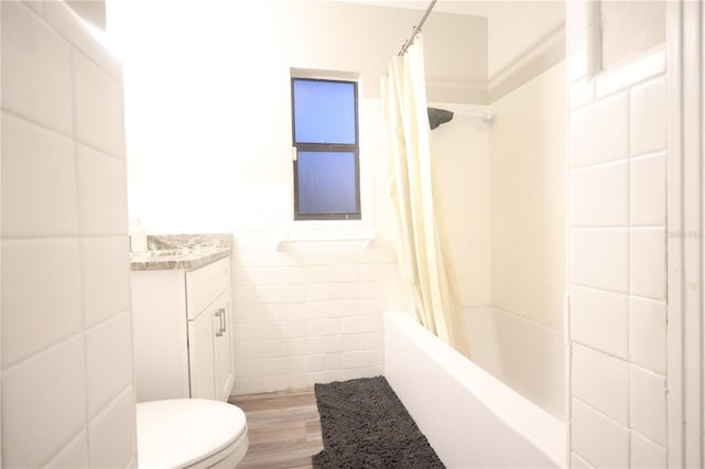 bathroom with toilet, wood finished floors, shower / bathtub combination with curtain, vanity, and tile walls