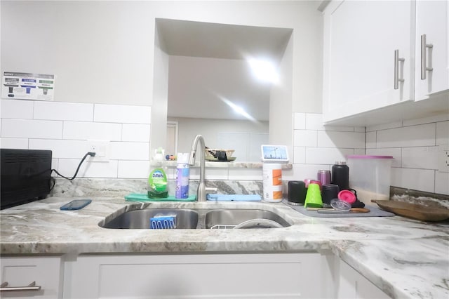 kitchen featuring light stone counters, white cabinets, and a sink