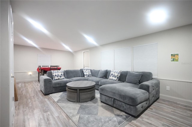 living area with light wood-type flooring, a wainscoted wall, baseboards, and vaulted ceiling