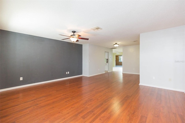 empty room with baseboards, visible vents, ceiling fan, and wood finished floors