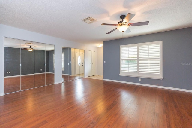 unfurnished living room with a ceiling fan, a textured ceiling, visible vents, and wood finished floors