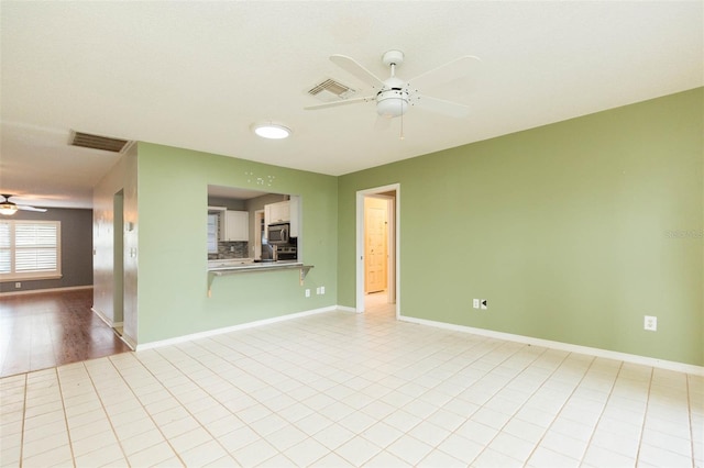 unfurnished living room with a ceiling fan, visible vents, and baseboards