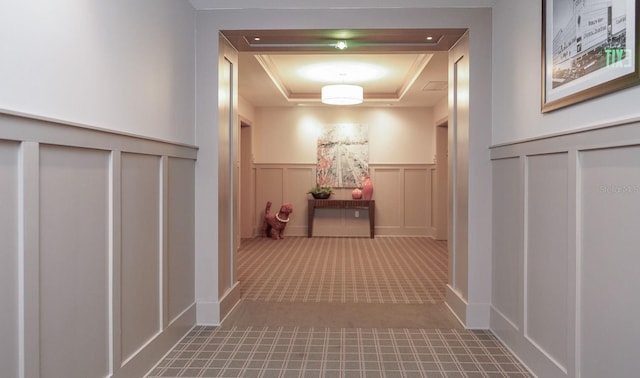 hallway with a wainscoted wall, carpet, a raised ceiling, and a decorative wall