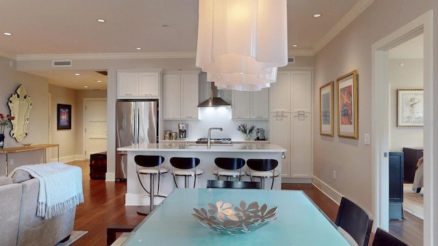 kitchen featuring visible vents, light countertops, wall chimney range hood, freestanding refrigerator, and a center island with sink