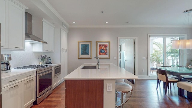 kitchen with stainless steel appliances, light countertops, wall chimney range hood, dark wood finished floors, and crown molding