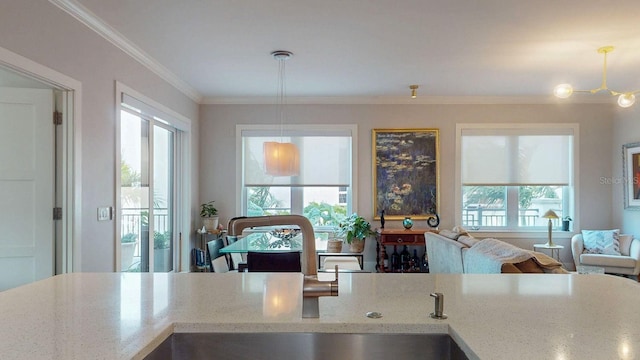 kitchen with ornamental molding, open floor plan, decorative light fixtures, light stone countertops, and a sink