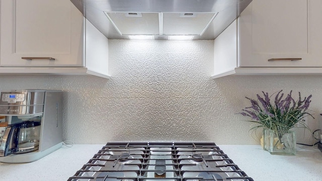 details featuring a textured wall, light countertops, ventilation hood, and stainless steel gas stovetop