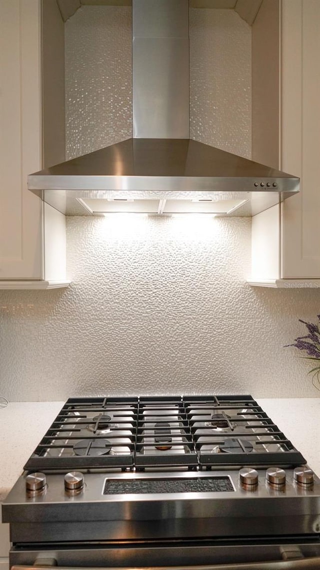 room details featuring light countertops, wall chimney range hood, stainless steel range with gas stovetop, and decorative backsplash