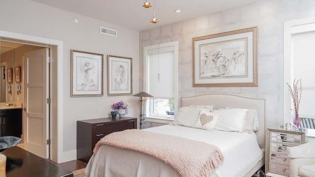 bedroom with a sink, ensuite bath, visible vents, and wood finished floors