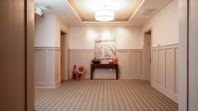 hallway with a tray ceiling, visible vents, and a decorative wall